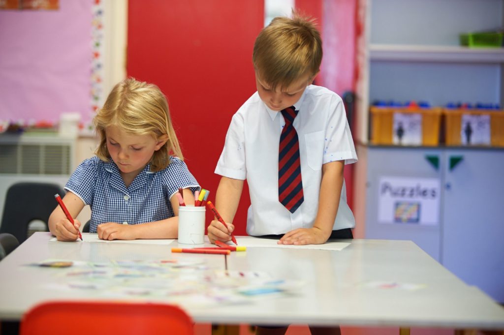 Two students are pictured colouring on a sheets of paper beside one another.