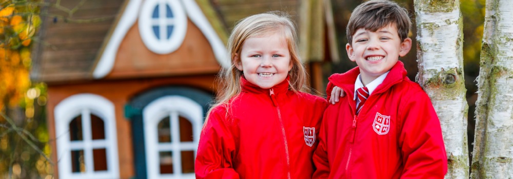 Two students smiling while standing next to a tree in the school playground