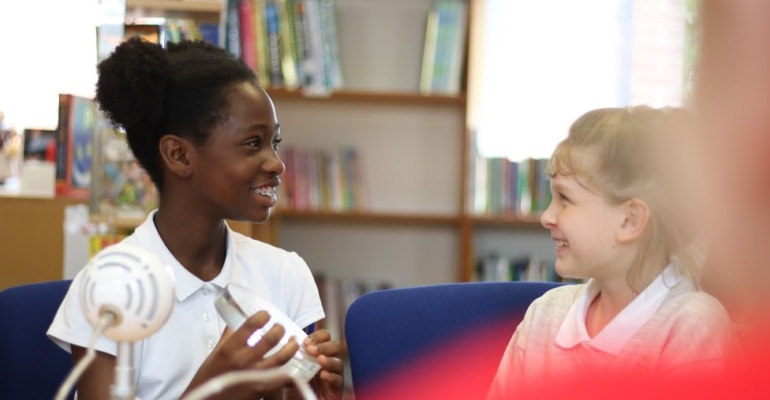 Two students smiling at each other while sitting on a chair in the school library.