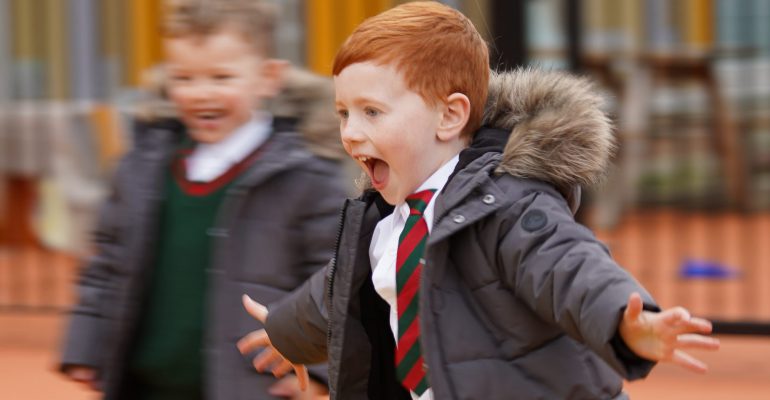 A young boy in a school uniform smiling while running through the playground.