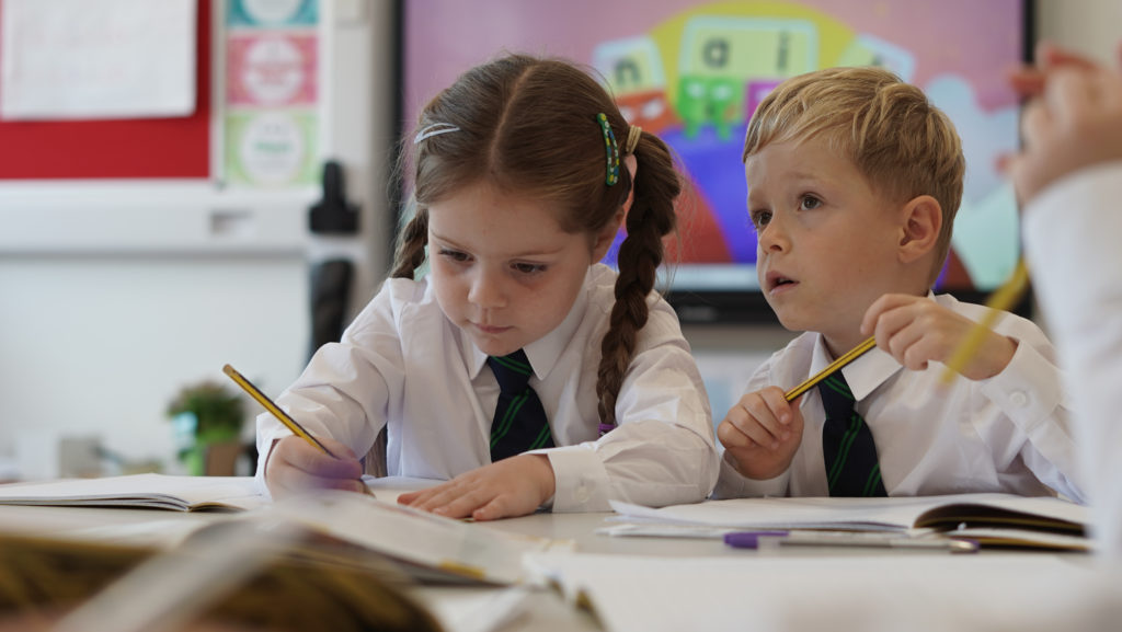 Two young students writing in a book during a lesson in a classroom