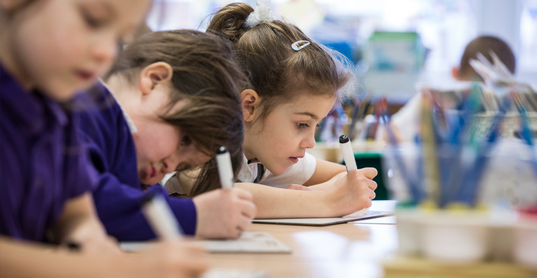 Three female pupils are seen sitting at a table together, making notes during a lesson.