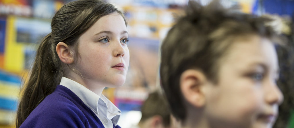 A young girl seen looking up at the whiteboard in a classroom, during a lesson.