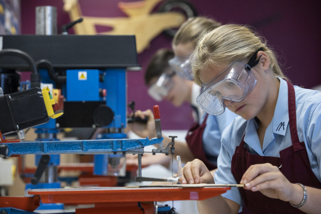 A young student wearing safety googles while using a electric saw during a design and technology workshop