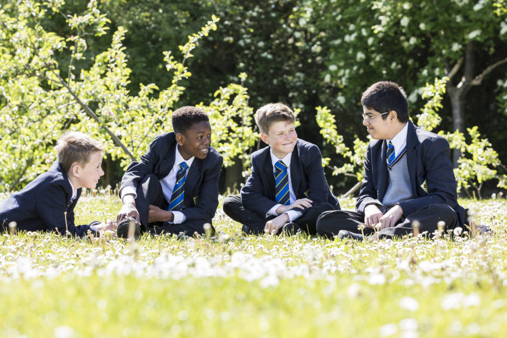 4 school boys sitting on the ground in a field holding iPads