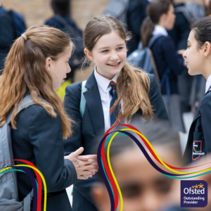 Three school girls talking to each other. A girl in the centre of the photo is smiling at another girl.