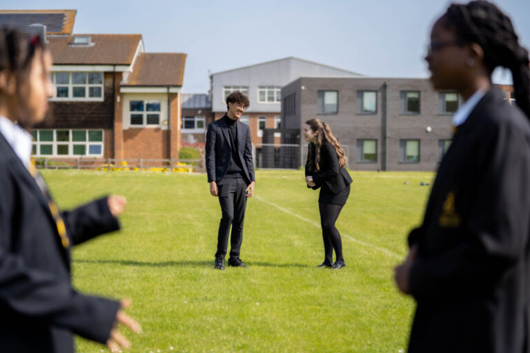 Two post 16 students talking with their school in the background.