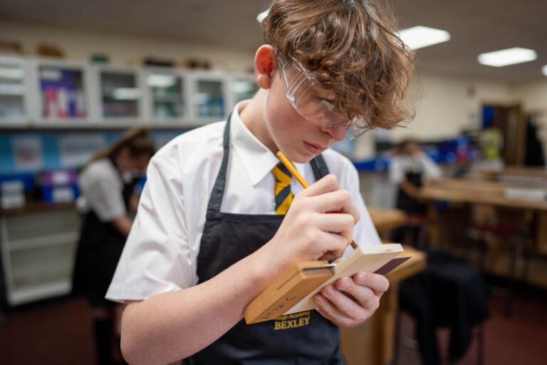 A engineering student marking a bit of wood with a pencil.