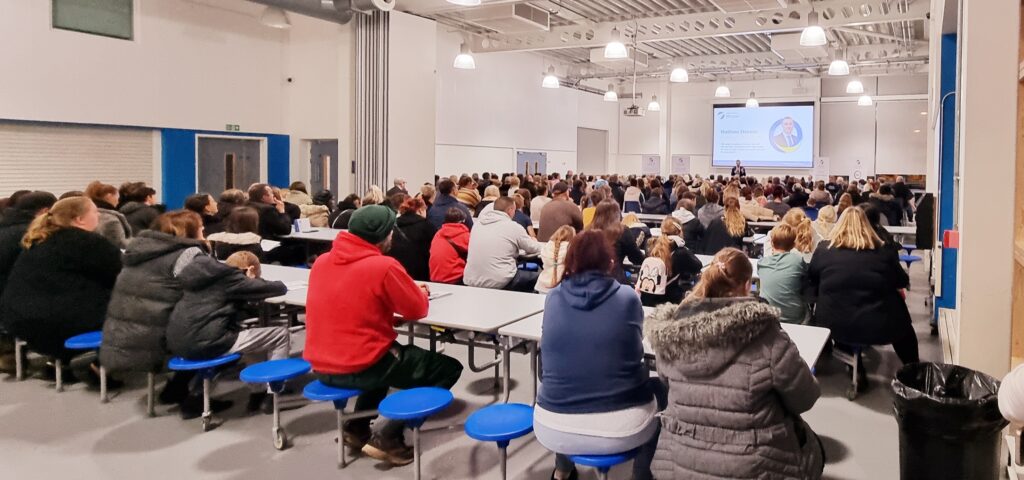 A hall full of parents and prospective students with a speaker at the front.