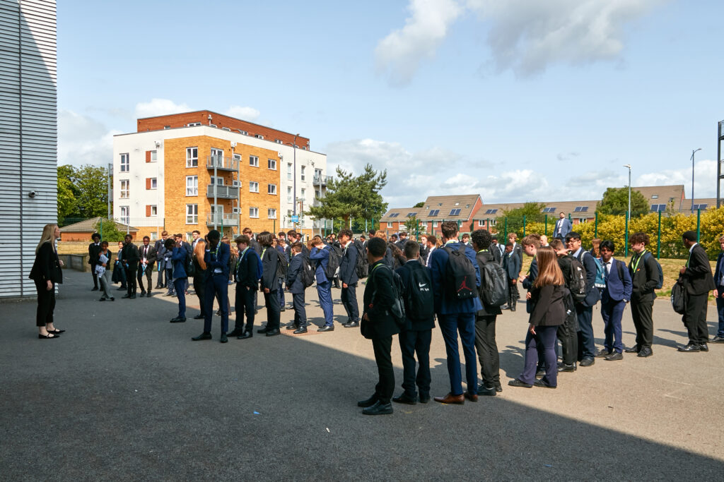 Pupils in five rows line up in the playground while a teacher speaks to them