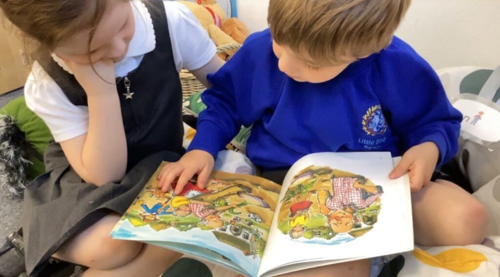 Two young school children sitting down together looking at a book with colourful illustrations