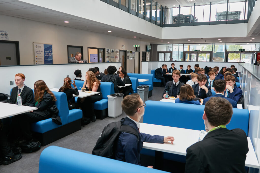 Pupils of Leigh UTC sitting in the school canteen. An teacher is chatting to one group.
