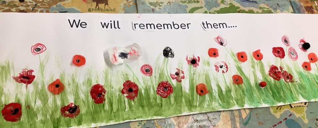 A strip of artwork on paper with painted green grass and red poppies. The text above the artwork reads: "We will remember them."